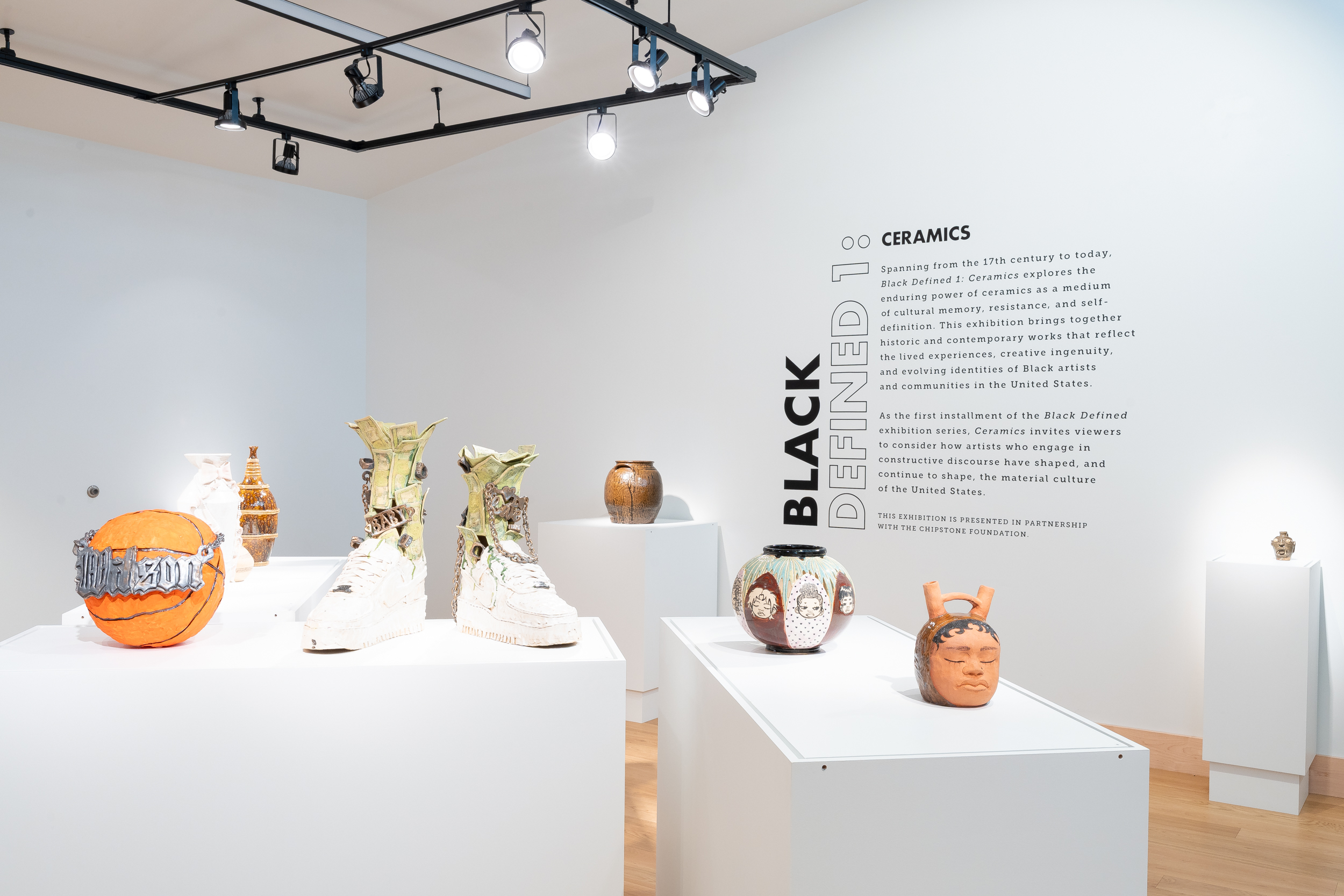 Installation View, “Black Defined 1: Ceramics,” 2025. Milwaukee’s Bronzeville Center of the Arts. Ceramic works on pedestals paired with the intro text on a white wall. Photo: Daniel McCullough.