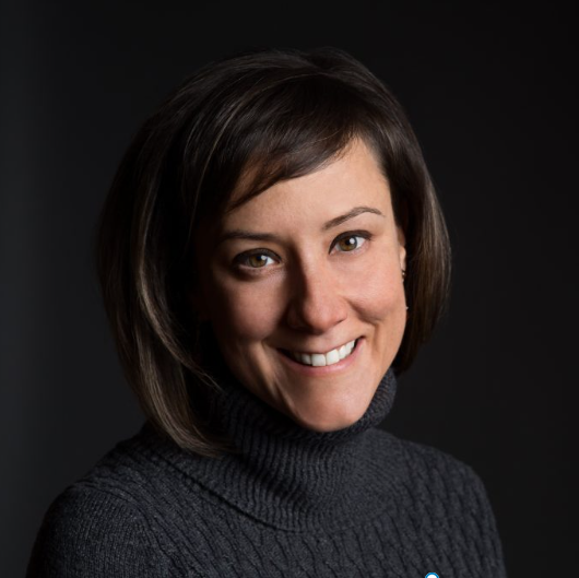 Maggie Andersen headshot. Maggie has short dark hair and is wearing a charcoal turtleneck. She sits in front of a dark background. Image credit: Claire Demos.