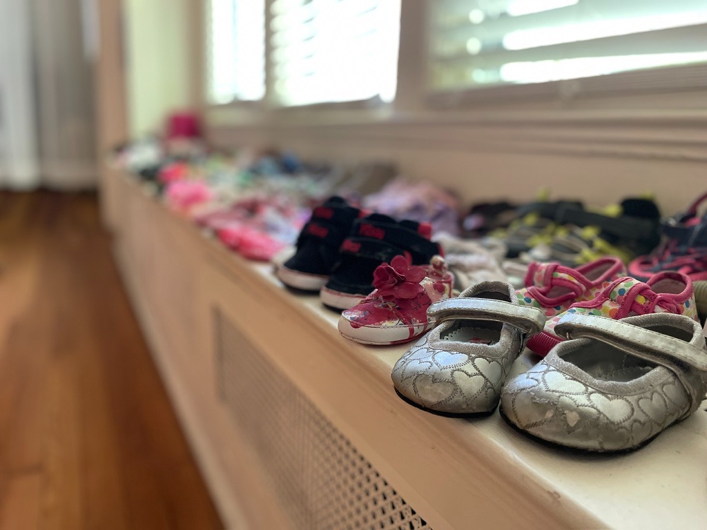 Image: Close up of dozens of children's shoes sitting on a bench beneath windows. First conceived in 2024 and exhibited at the James and Grace Lee Boggs Center, Bury Your Love Around Us is part of a larger installation which uses 400 pairs of children’s shoes to honor the lost children and families of Palestine. It includes sound recordings of the names of the deceased children. The full piece invokes interactive collective mourning through a series of acts and time for reflection. Photograph by Irina Zadov.
