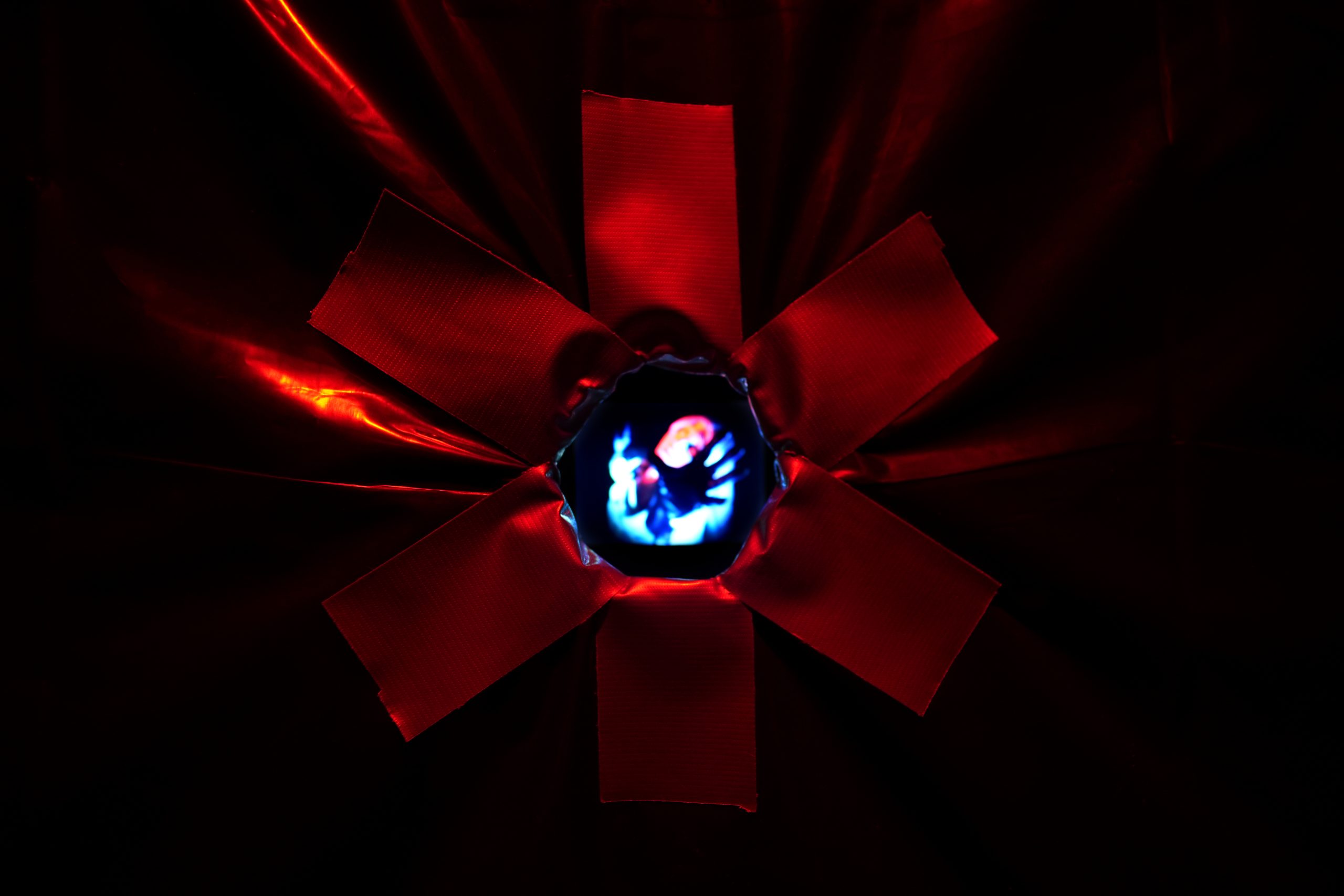 An indistinct, eerie performer is visible through a glory hole lined with duct tape. Photo courtesy of the artist.