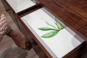 Image: Temitayo Ogunbiyi, “You will find new framing in crafts of old,” 2023. A hand pulls open a drawer. Inside is a painting of green leaf-like shapes on white paper. Commissioned by the Museum Tinguely. Photograph by Bettina Matthiessen.