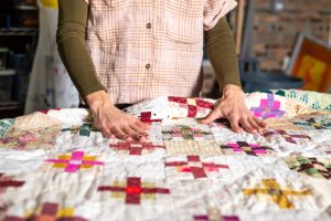 A pair of hands smooth out a quilt with a colorful, geometric pattern. Image by Tonal Simmons.