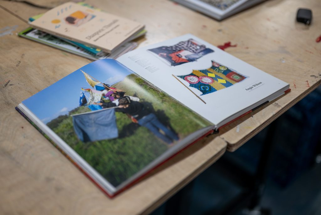 A close-up image of an open book with photographs of quilts and a group of people carrying flags through a field. Image by Tonal Simmons.