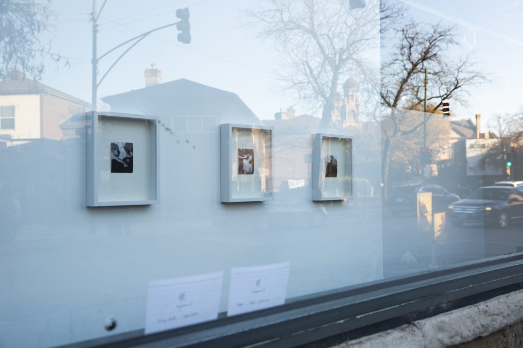 Index cards stuck against the glass from the inside of the window. From left to right: Untitled (Being Maya’s Mother), Untitled (Being Kamille’s Mother), Untitled (Being Madi’s Mother), from the series Mother Figure by Kat Bawden and index cards from Ruby Que’s Cantonese lessons, 2025. Viewed from the storefront window of Roots & Culture, photograph by Kat Bawden. Three black and white photographs in white frames hung up on a wall viewed through a glass window with reflections of a street. 