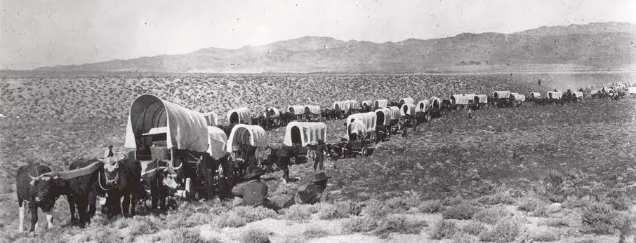 A black and white photograph of covered wagons traveling the Oregon trail.