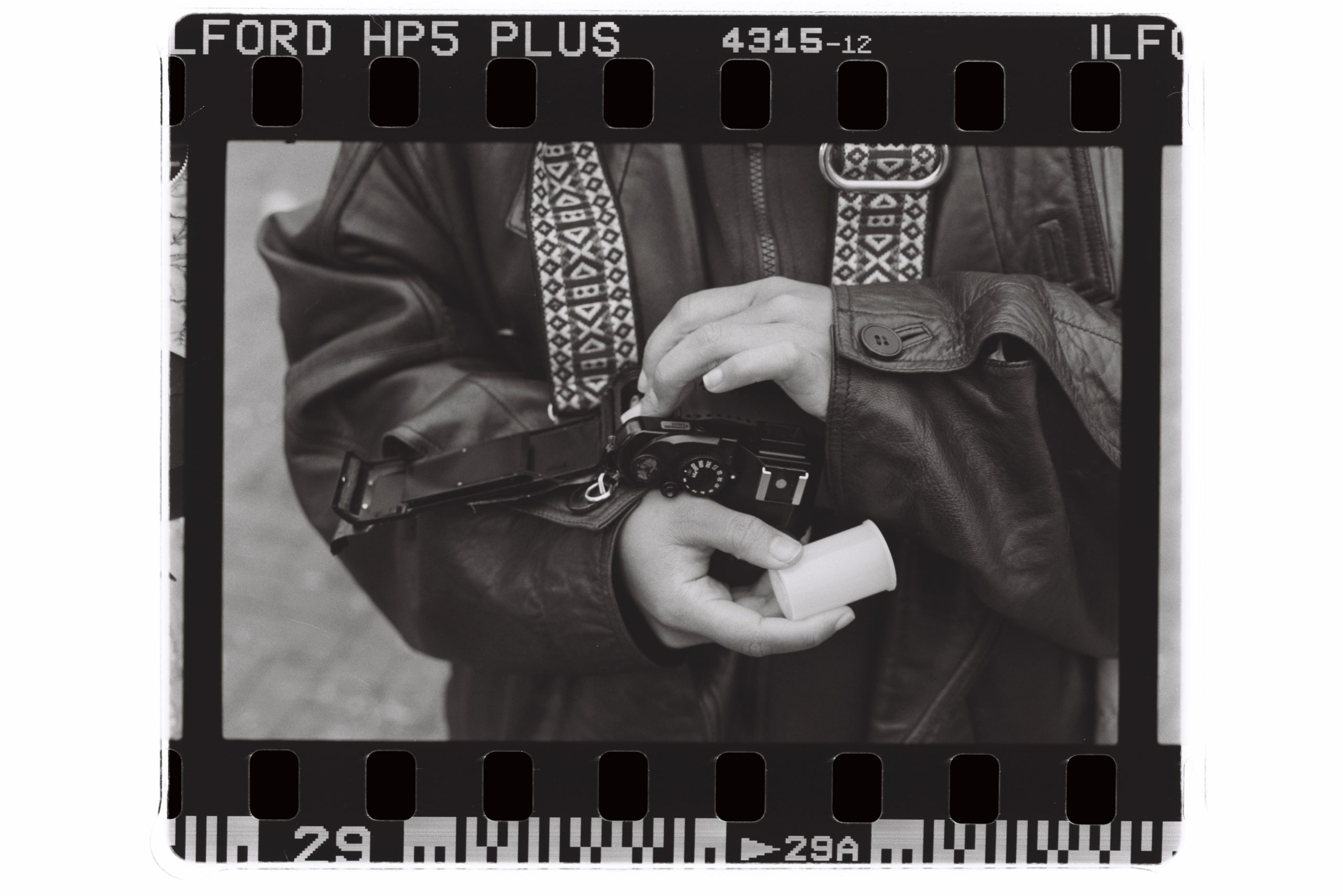 A black and white film scan captures photographer Han on cam holding their camera. Photo by Genesis Falls.