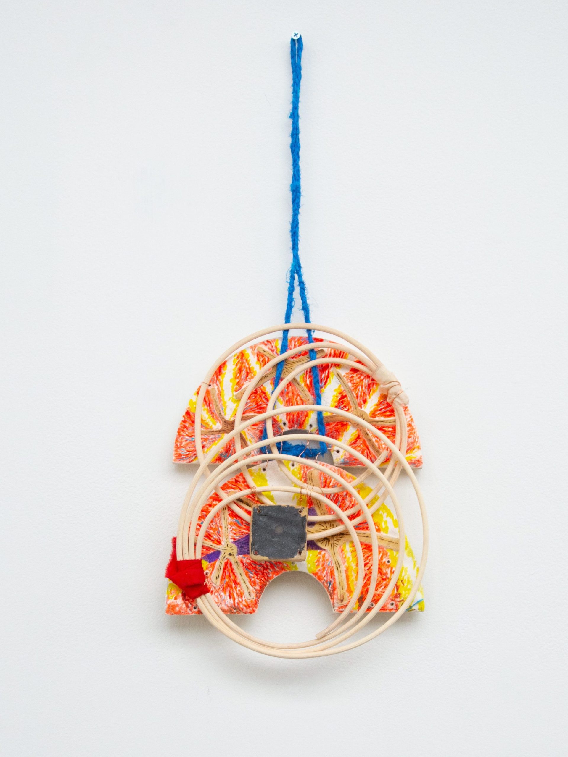 Sending a Picture (broken bi), 2026. A sculptural form hangs from the wall fabricated from a long rope made from blue silk, two half crescent fresco pieces, a small fresco tile, and several interlocking wooden circles. The pieces are tied together with a mixture of red ribbon and copper wire.