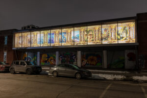 Installation view of Amay Kataria’s Saṃsāra shown behind glass windows above a car filled lined street at Hyde Park Art Center on a winter's day. Saṃsāra consists of a series of AI-generated digital paintings depicting scenes reminiscent of life on Earth in the past, present and future. The images include plant life, two people seated in viritual reality helmets, a plane taking off and a woman and child sitting faced each other in a forest. Image by Amay Kataria.