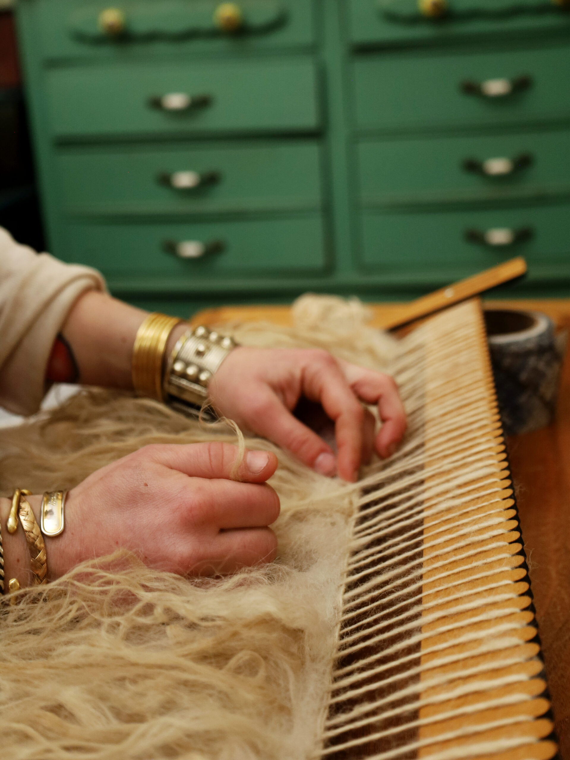 A close-up of Rachel's wrists and hands while weaving the Varafeldur piece. There is a teal dresser in the background. Image by Viki Stark.