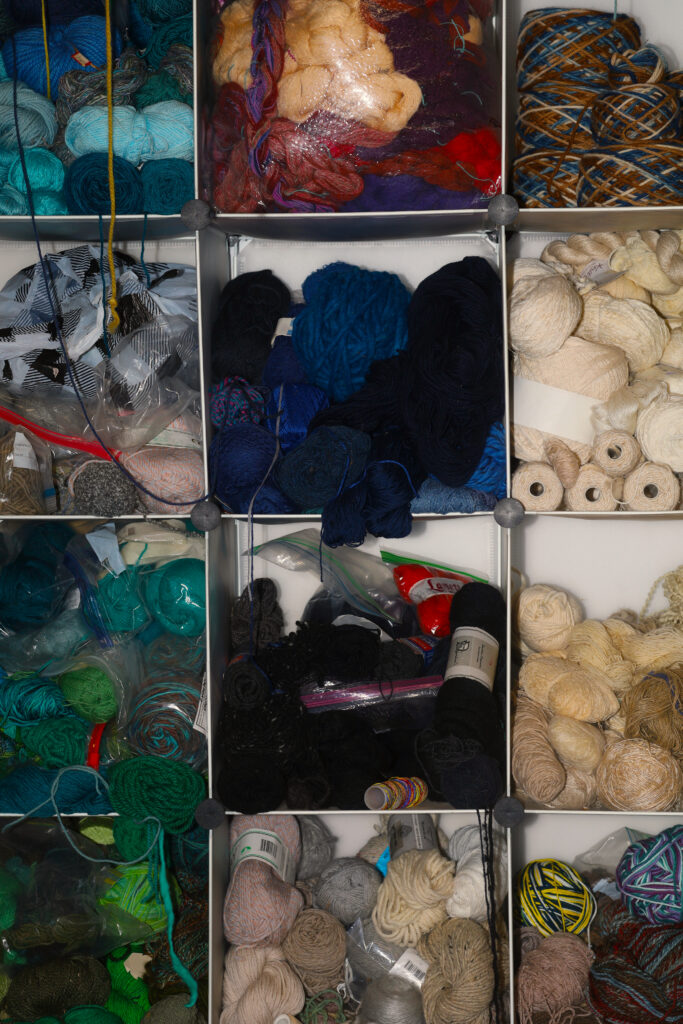 Detailed shot of the studio’s yarn wall. Hundreds of skeins, tightly wound or otherwise, are separated by color in dozens of stacked square shelves. Populated with mostly wools, but also crochet cottons, jute, and hemp yarns gifted to Rachel by other weavers, grandparents, friends of family members, and occasionally even regulars at the brewery where she works. Image by Viki Stark.