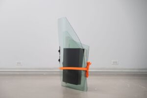 Una vista central de Calle West Pershing y Avenida Sur Campbell (Cuidado Preventivo) La escultura consta de cuatro cristales de ventanilla de carros de color azul-verde con cuadrados de espuma de poliuretano entre cada uno. Una correa de trinquete naranja la rodea y la escultura se apoya directamente en el suelo. Documentación por Negin Mirfakhraee.