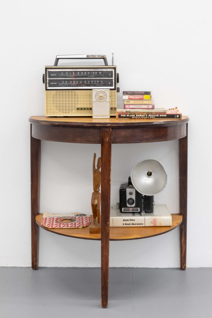 An installation view of: Jen Everett, Untitled, 2023. A vignette made up of a table, books, vintage audio equipment, and other various objects. The installation were on view as part of the exhibition Beneath the City, a World at The Luminary. Photos by Emily Mueller, courtesy of The Luminary.