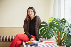 Crystal Vance Guerra sits on a bench in the front room at Tala Gallery with a stack of books at her side. Image by Kristie Kahns.
