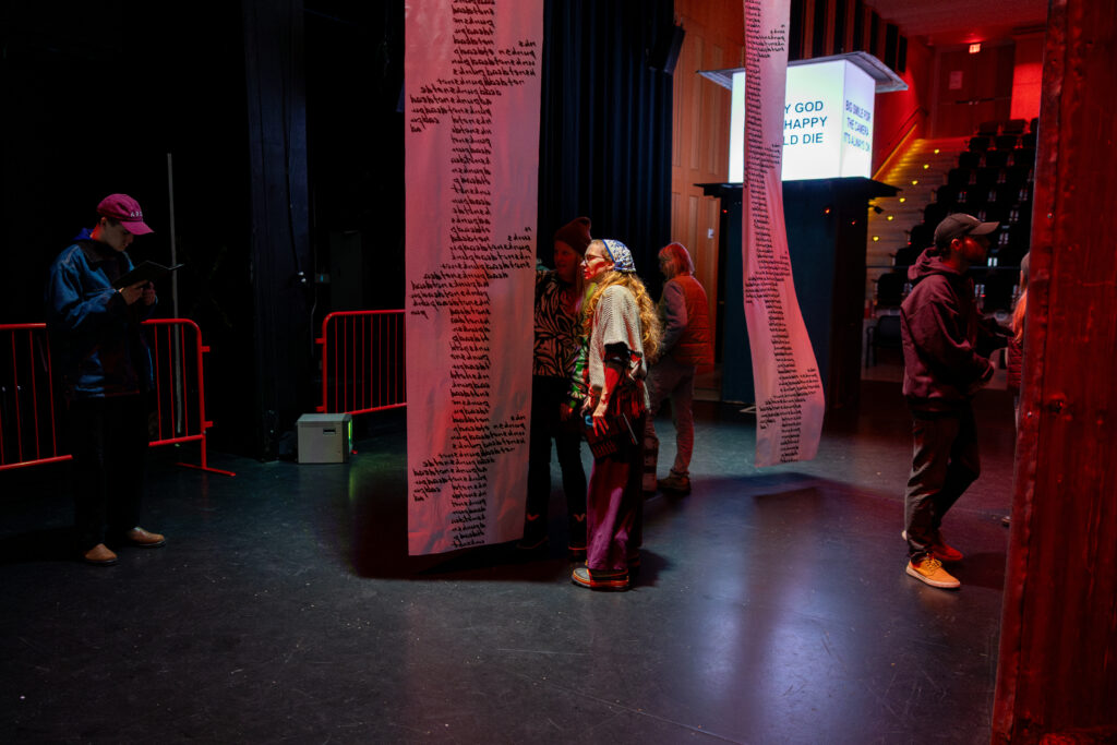 An installation view of POLICE STATE by Nadya Tolokonnikova at MCA Chicago. Museum goers inspect hanging scrolls adorned with handwritten script. Image by Alexis Ellers.