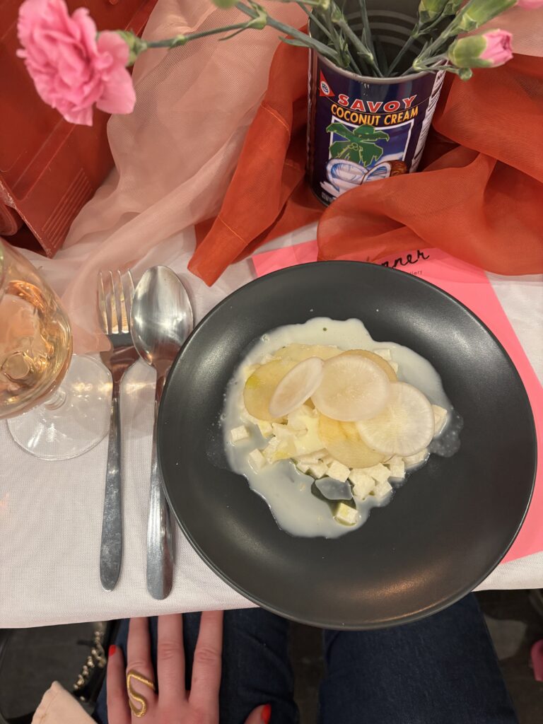 Image (right): A diner's view of the third course at Girl Dinner (radish, daikon, apple, cheddar, white chocolate, and a touch of habanero). Bright pink flowers and pink menus can be seen nearby. Image courtesy of Ally Fouts.