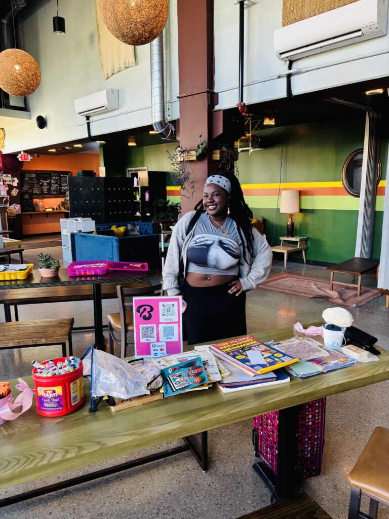 A photo of Ladasia Bryant smiling behind a table at Milwaukee Zinefest. Photo courtesy of the author.