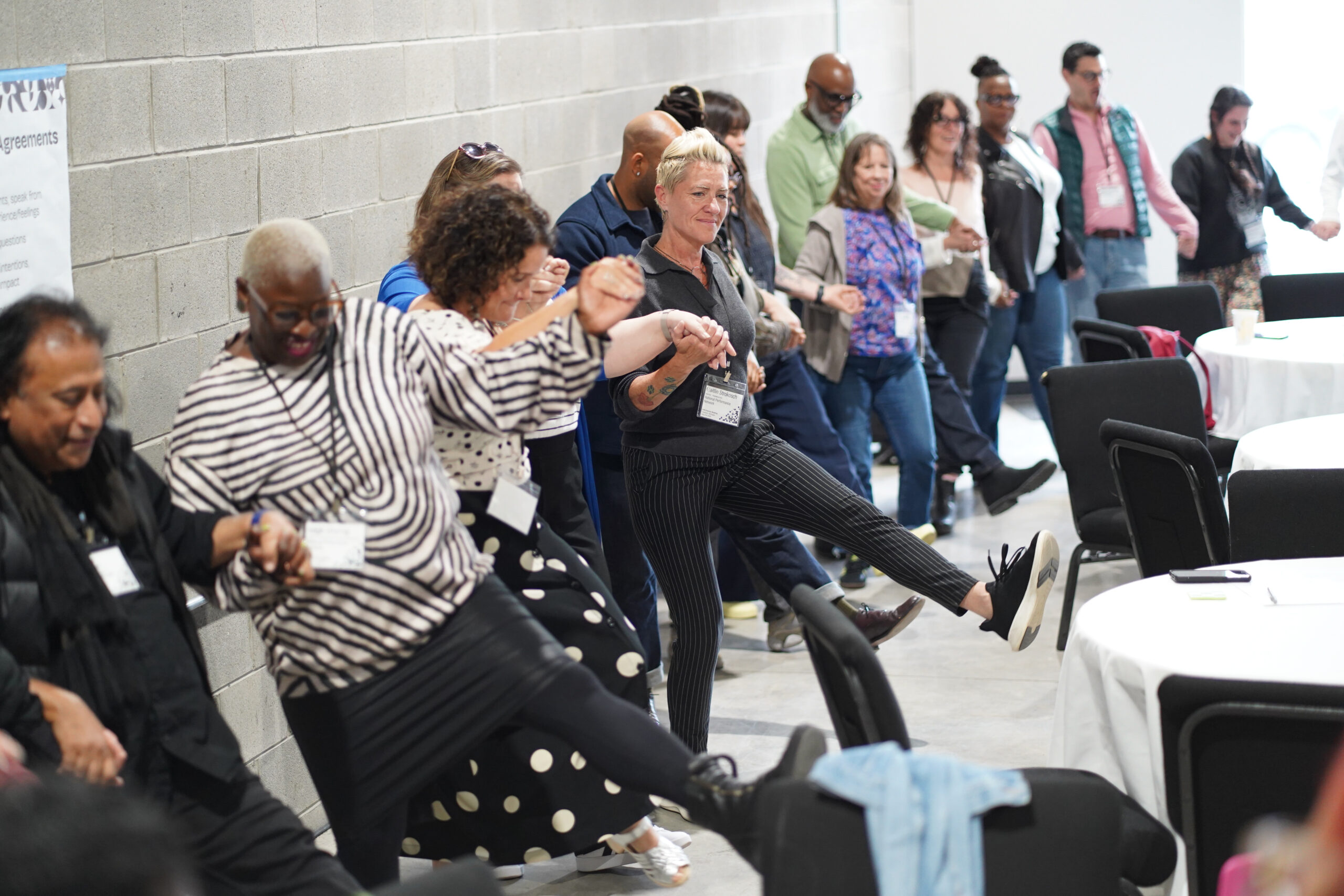 Attendees at the National Performance Network's 2026 Partner Meeting at the Arab American National Museum in Dearborn, MI practice dabke around the edges of a conference room. I