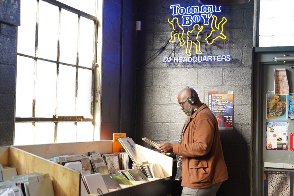 An attendee of NPN's Community Reception at Spot Lite Detroit inspects a record they have pulled from a bin. They are wearing over-the-ear headphones and a brown cardigan. 