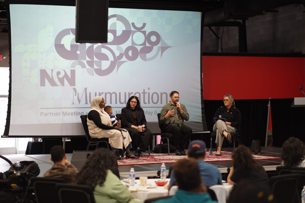 Detroit-area artists Layan Srour, Raphique Barakat, and Khadega Mohammed are seated onstage in front of an audience for a discussion moderated by AANM’s Director Dr. Diana Abouali. Behind the artists there is a projector screen with NPN's logo, a graphic image, and information about the Partner Meeting, including the theme, "Murmurations."