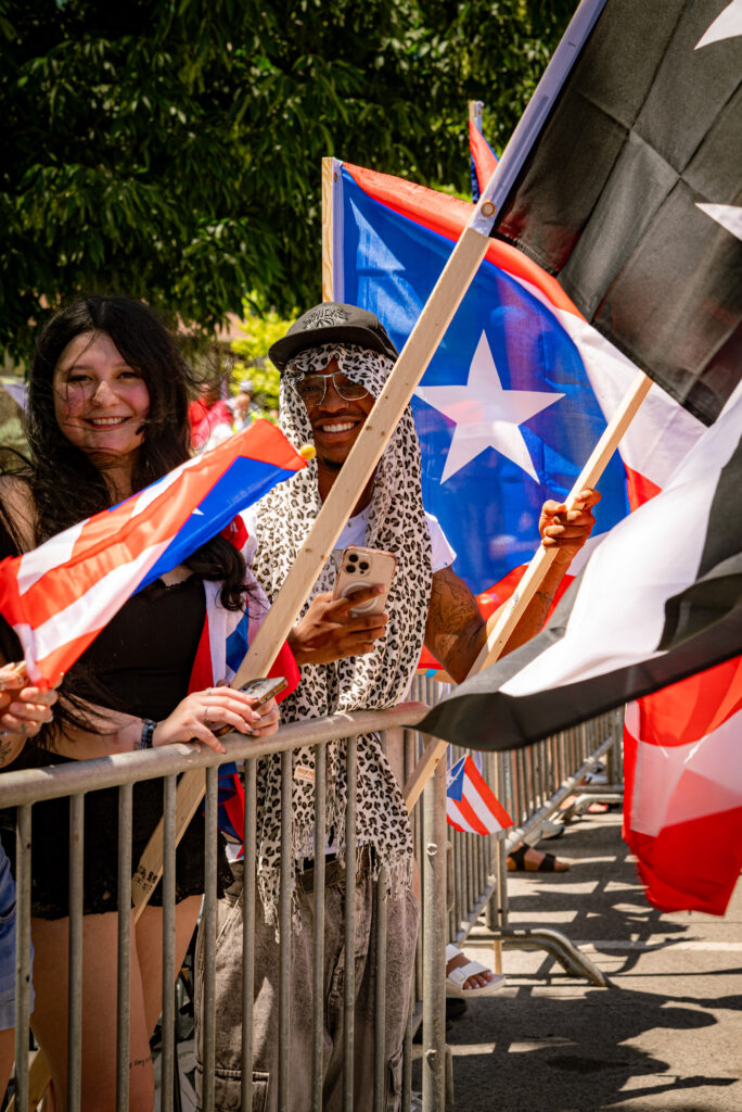 Crowd members smiling, holding the black and white Puerto Rican flag. Photo by Tonal Mondae.