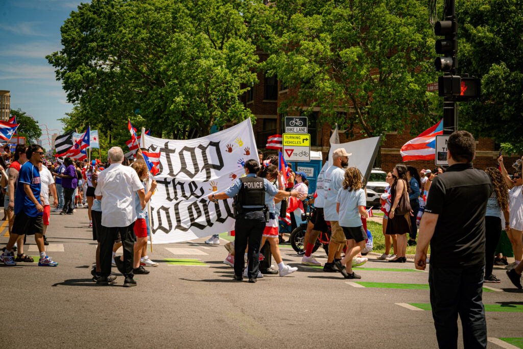 The marchers hold a sign that says “Stop the Violence” as a police officer ushers them to turn off of Division towards the end of the designated parade area. Photo by Tonal Mondae.