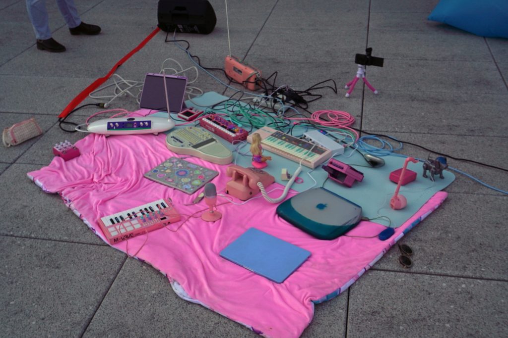 An assortment of technology and music items on a pink blanket. Photo courtesy of the artist. 