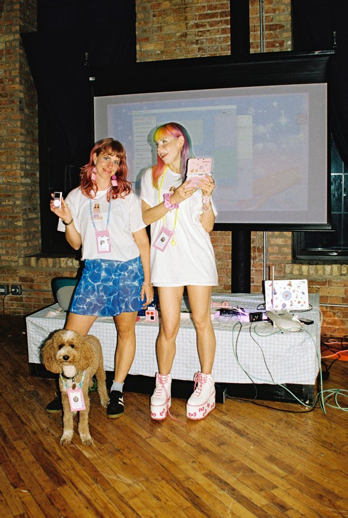 Zsofi Valyi-Nagy and Clara Venice posing in front of a table of music and electronic equipment with a dog. Photo courtesy of the artist.